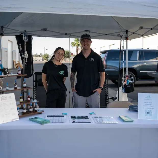 Two Flow IV team members behind their branded table at an outdoor event.