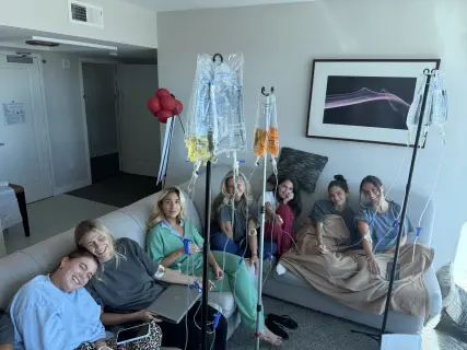 A group of friends receiving IV therapy together on a hotel suite sofa.
