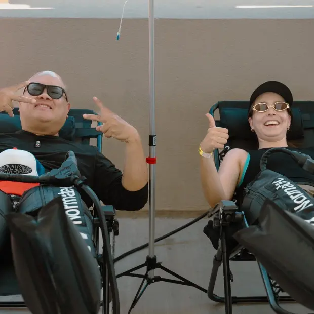 Two clients relaxing in recliners with compression boots and an IV drip at a Flow IV event.